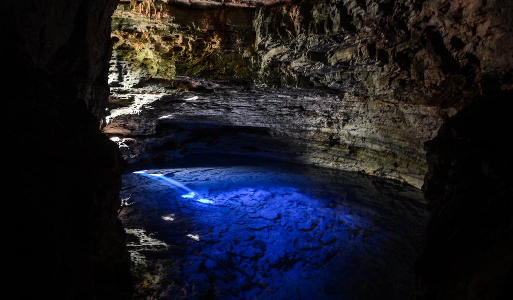 The blue underground lake of Poço Encantado lit by a shaft of sunlight